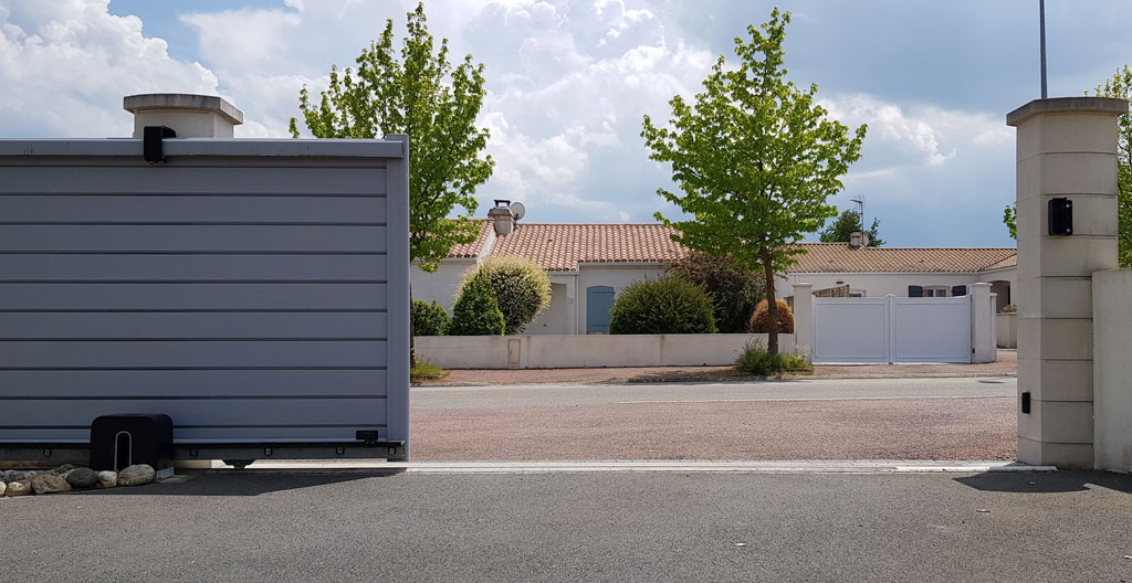 Vue plongeante sur une allée gravillonnée en pente douce menant à une entrée de propriété, végétation bretonne sur les côtés
